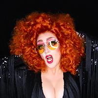 A woman with curly red hair, large amber glasses and bright red lips