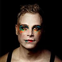 A man with bright multi-coloured makeup around his eyes and lips