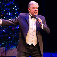 A man sings big in front of a lovely Christmas tree.