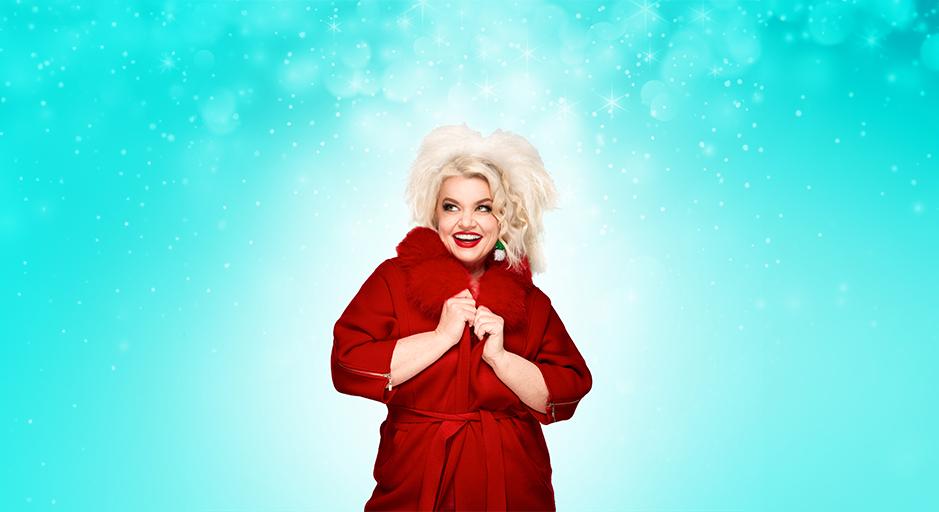 A blonde woman stands in a red coat surrounded by fake snowflakes
