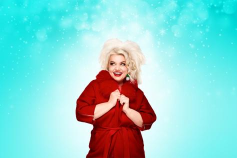 A blonde woman stands in a red coat surrounded by fake snowflakes