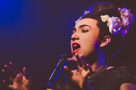 A performer with flowers in their hair sings close to a microphone