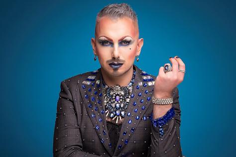 A performer with a jewelled suit, and dramatic makeup stares at the camera. 