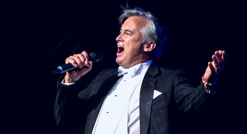 A man in suit sings with his arm stretched out. 