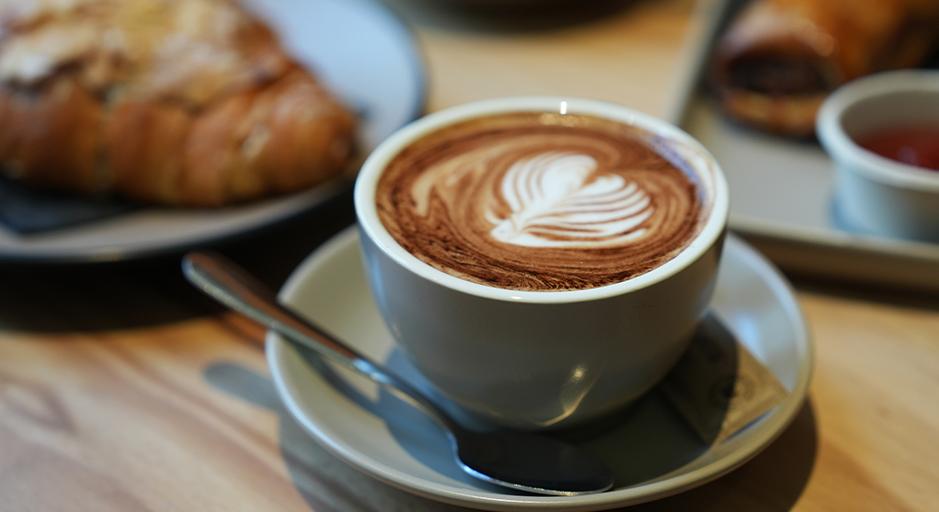 A coffee in a cup, with a croissant in the background. 