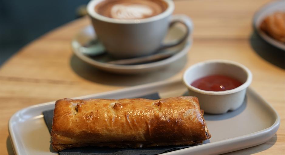 Sausage roll on a plate, with a coffee in the background